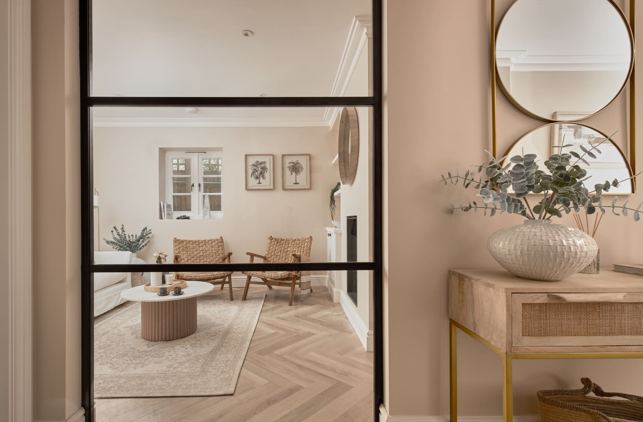 Staged home hallway looking into living room through glass partition. Mirrors, plants and decorative ornaments adding detail to the designer furniture and artwork on display in this Tunbridge Wells home.